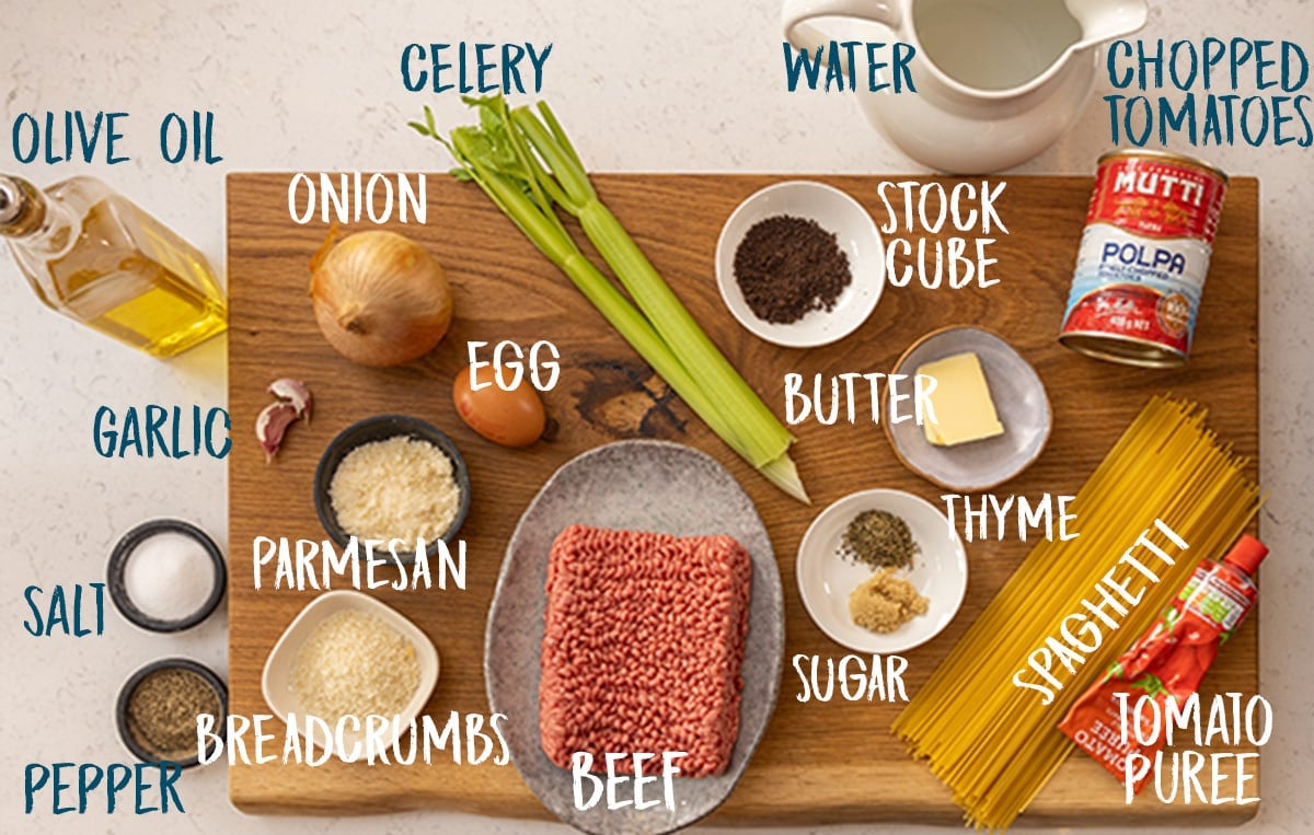 Ingredients for spaghetti and meatballs on a wooden board on a white background.