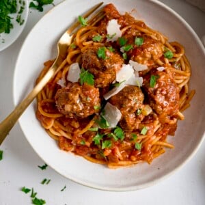 Spaghetti and meatballs in tomato sauce in a white bowl on a white background.  There is a golden fork in the bowl.