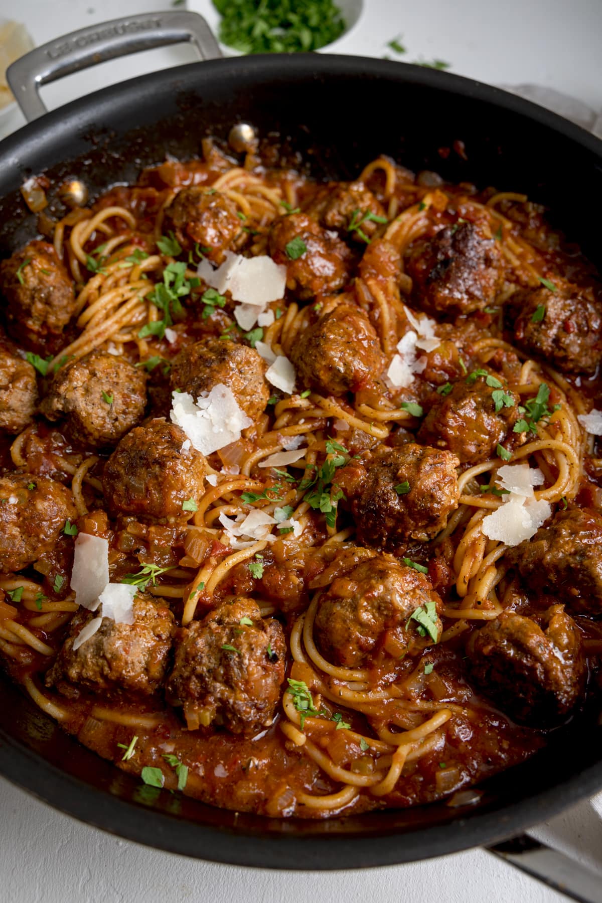 Close up overhead image of spaghetti and meatballs in a large pan on a white background.