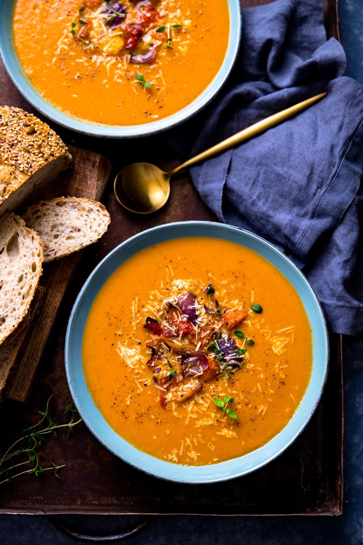 Roasted vegetable soup in a blue bowl with sliced bread and a spoon next to bowl