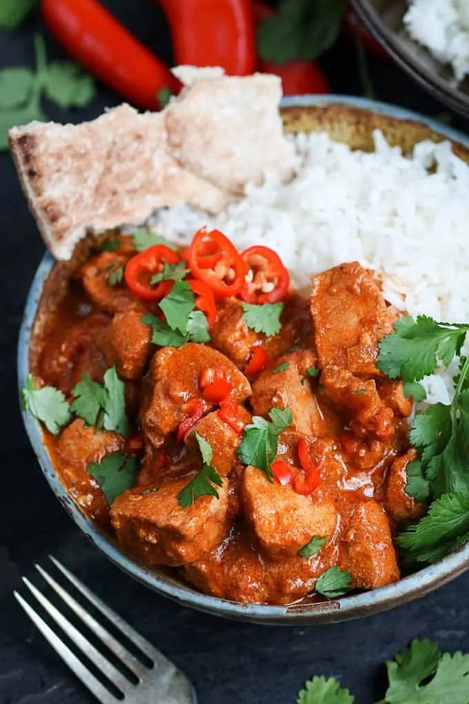 Slow-Cooked Spicy Chicken Curry with rice and naan in a stone bowl with chillies in the background and a fork in the foreground