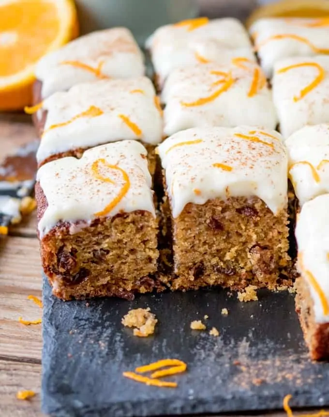close up of a fluffy moist carrot tray bake with orange infused raisins and zesty cream cheese frosting