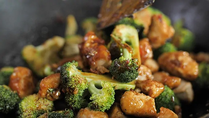 close up of asian crispy chicken and broccoli being stirred in a wok