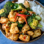 Square image of Asian crispy chicken with broccoli and rice in a stoneware bowl. Blue napkin in background