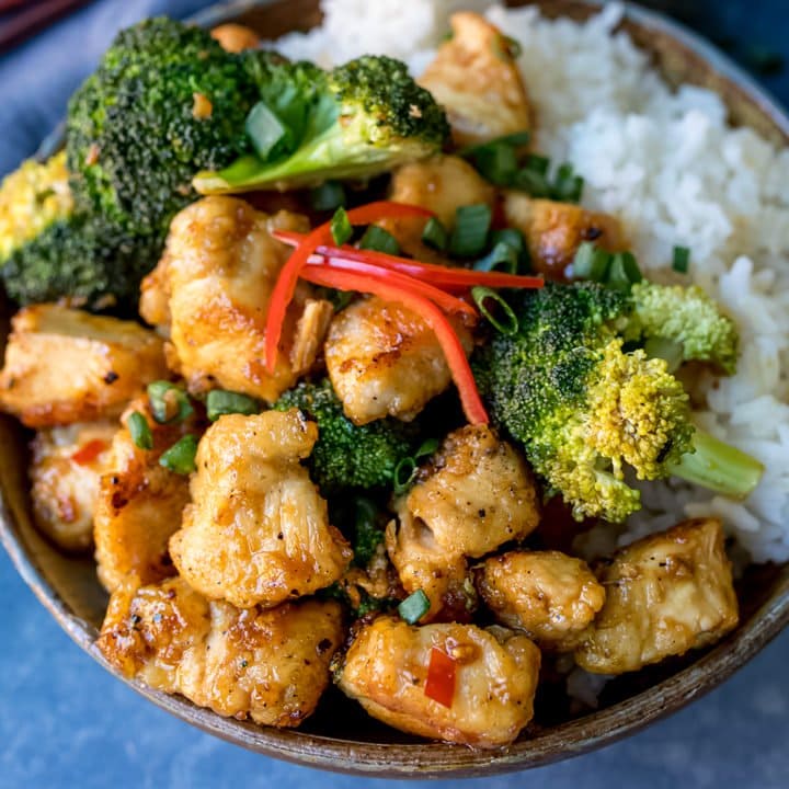 Square image of Asian crispy chicken with broccoli and rice in a stoneware bowl. Blue napkin in background