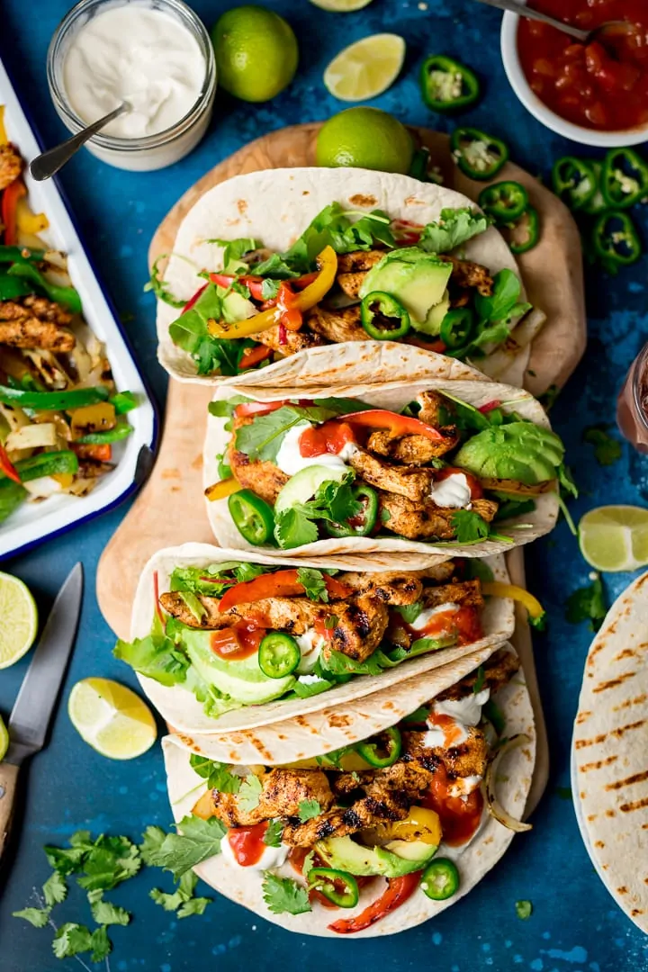 Overhead of chicken fajitas on a wooden board on a blue background