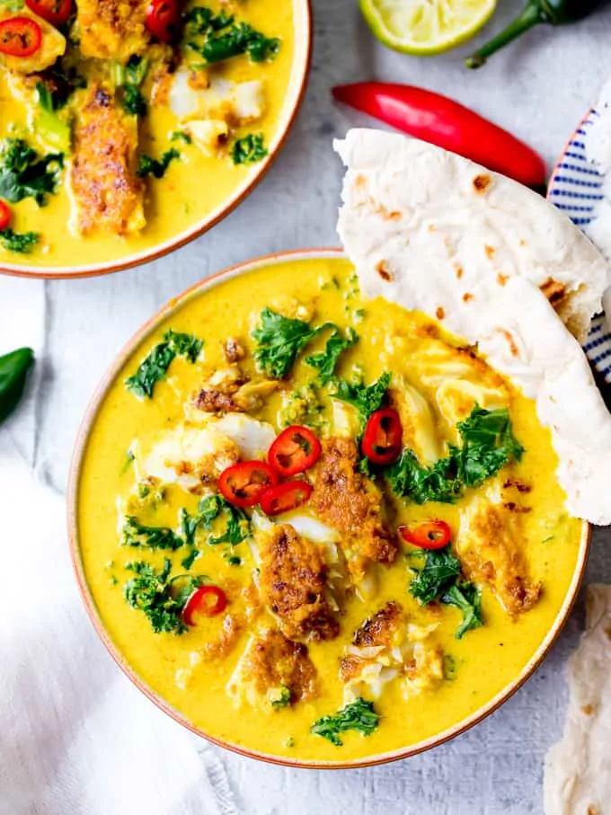 Overhead image of bowl of Thai fish yellow curry with kale and red chillies. Pita bread dipped in bowl.