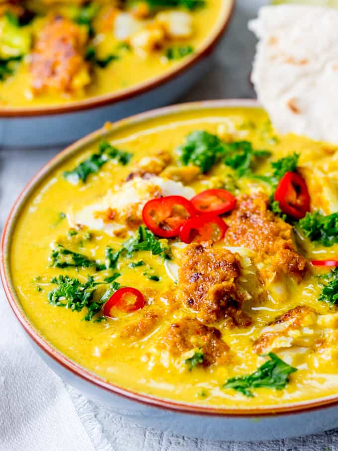 Bowl of Thai fish yellow curry with kale. Topped with red chillies.