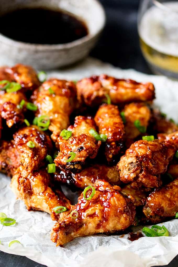 Portrait photo of Sticky and Crispy Asian Chicken Wings with a bowl of sauce and a glass of beer in the background out of focus