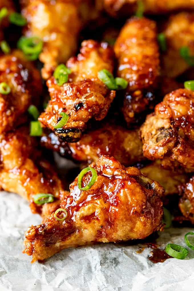 Close up picture of Sticky and Crispy Asian Chicken Wings glistening in the light stacked up on grease proof paper.