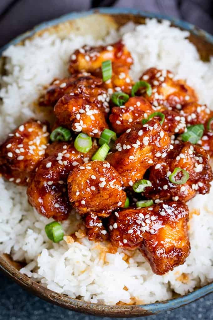 Close up photo of Crispy Sesame Chicken with a Sticky Asian Sauce on a bed of rice in a stone bowl with a dark background