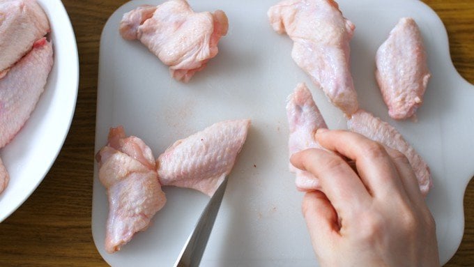 Chicken wings being cut into two pieces on a white chopping board