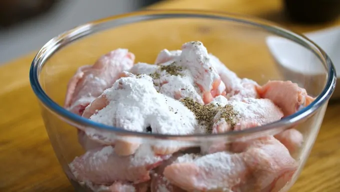 Raw chicken wings in a bowl with baking powder and seasoning