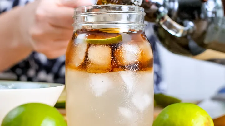 Pouring rum into a glass filled with ice and ginger beer