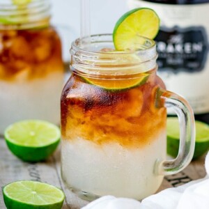 Mason jar glass filled with dark and stormy cocktail, topped with a slice of lime