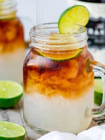 Mason jar glass filled with dark and stormy cocktail, topped with a slice of lime