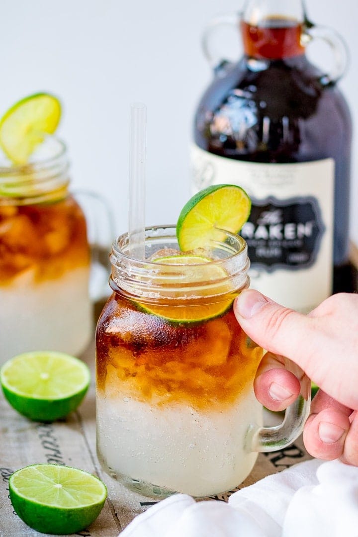 Photo of hand holding mason jar mug serving a dark and stormy cocktail with a lime garnish.