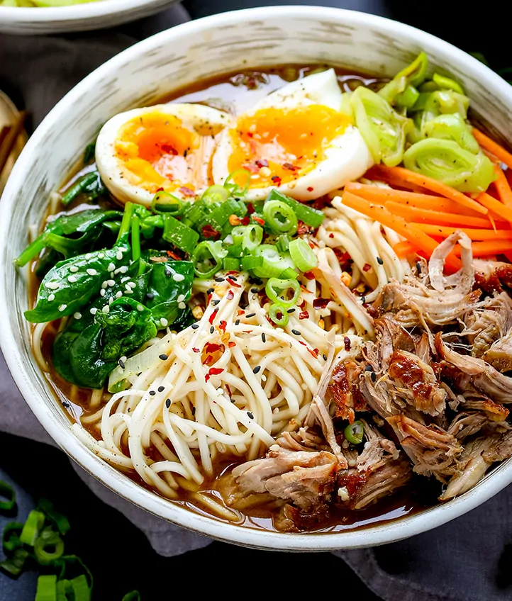 Close up photo of a bowls full of pork ramen with pulled pork, noodles, spinach, runny eggs and broth
