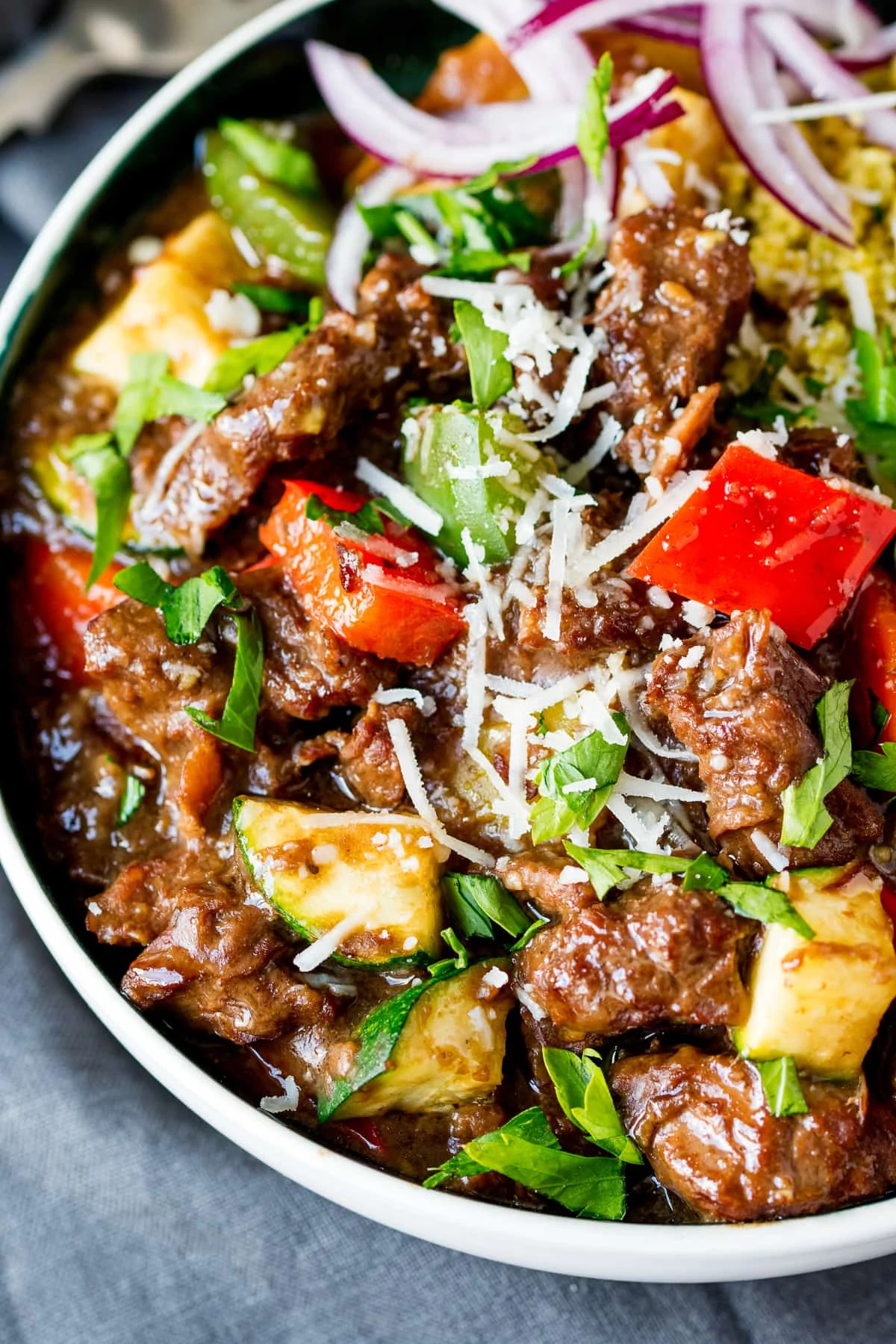 Close up overhead shot of summer beef casserole in a bowl with peppers, courgette and parmesan.