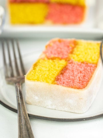 Battenberg cake slice on a plate with a fork on a light background.