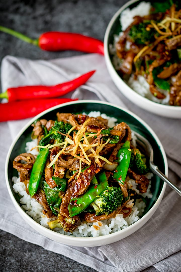 ginger beef with broccoli in a white bowl, topped with fried ginger