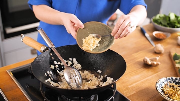 Garlic and ginger being added to a wok that has fried onions in it.