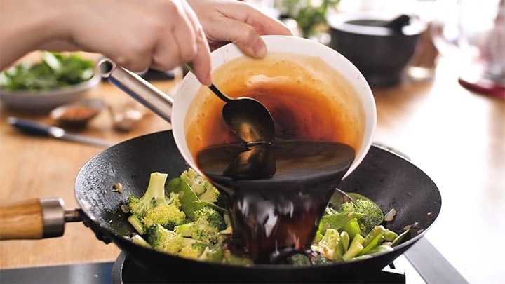 Stir fry sauce being added to a wok with broccoli and mange tout