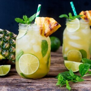 Pineapple Ginger Mojitos with Spiced Rum - a sweet and spicy twist on the classic mojito cocktail. Served with a wedge of caramelized pineapple.