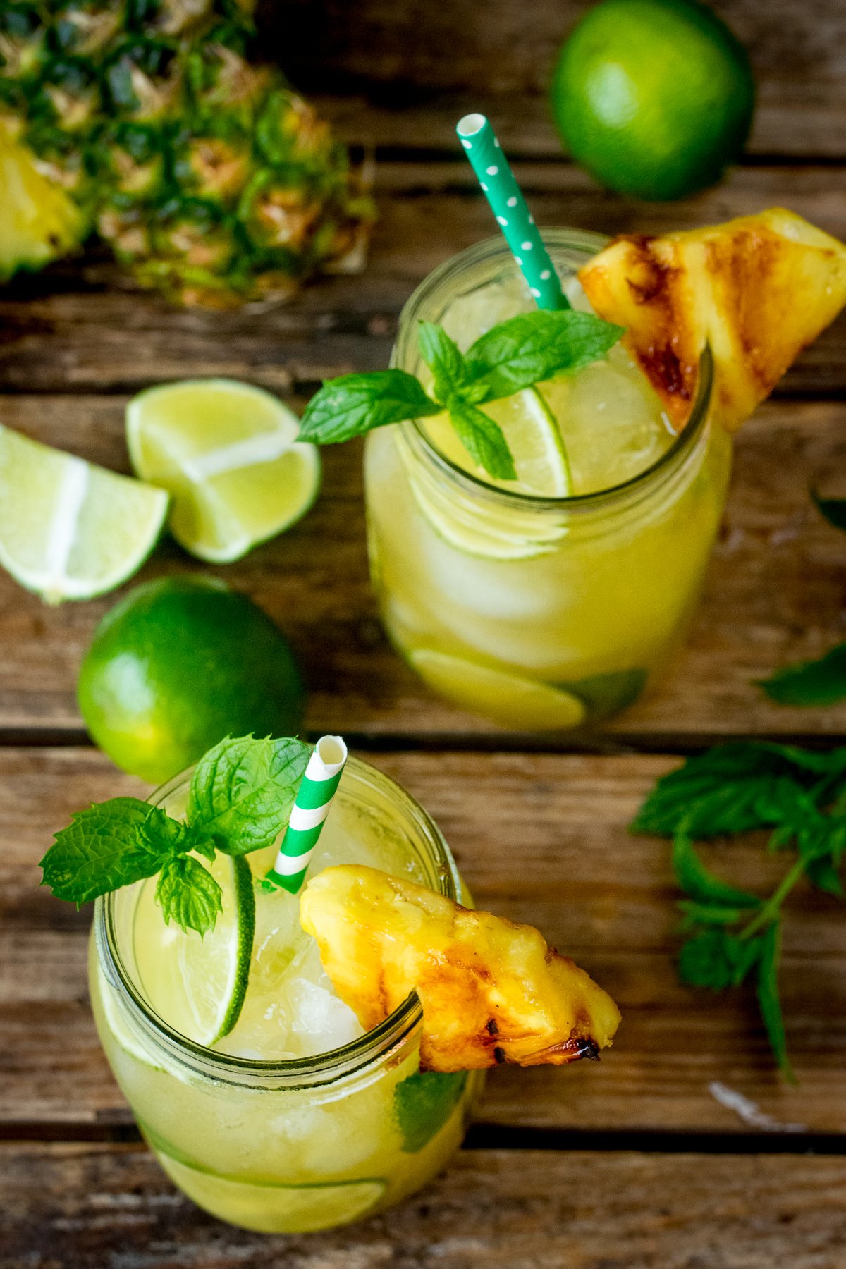 Overhead image of 2 mason jars filled with Pineapple Ginger Mojitos and decorated with mint leaves and caramelized pineapple.