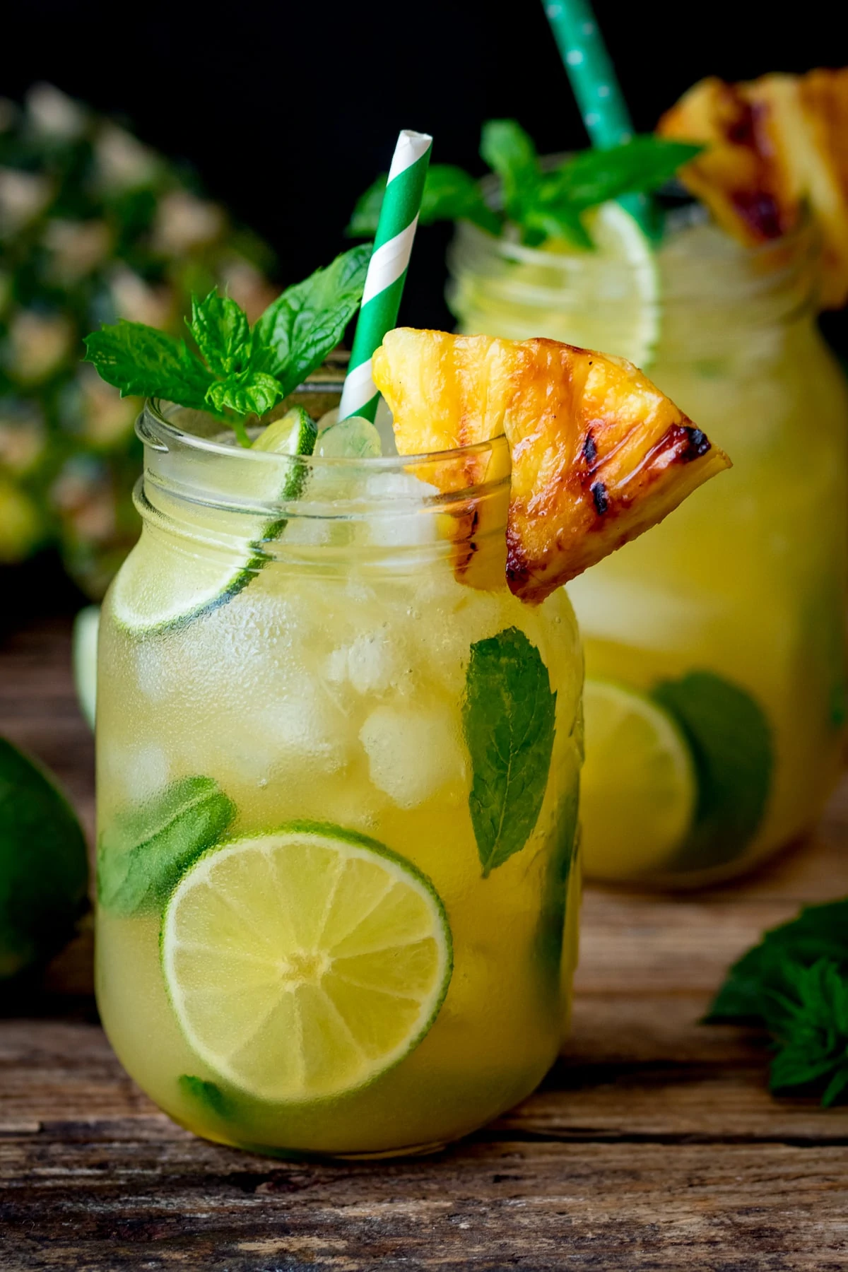 2 Pineapple Ginger Mojitos in mason jars decorated with wedges of caramelized pineapple.