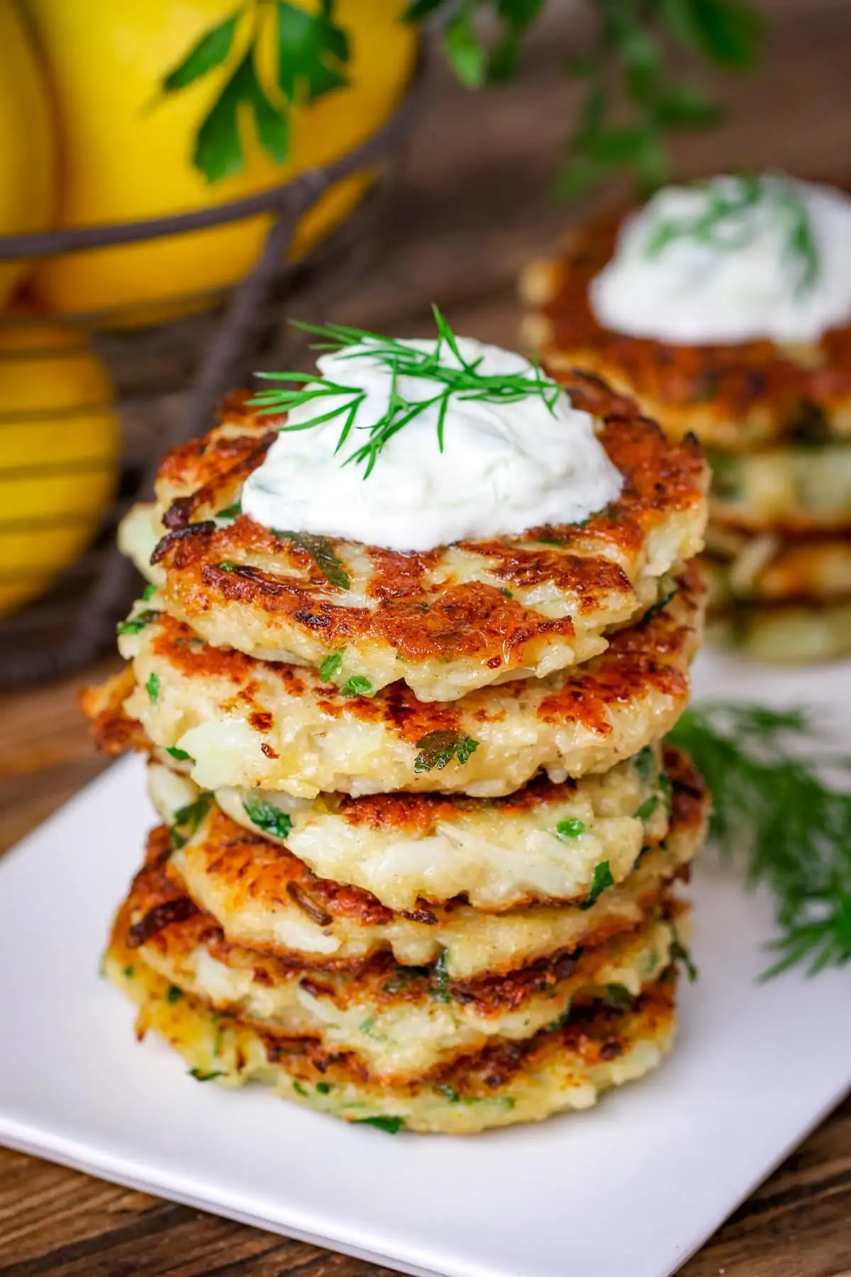 Stack of cauliflower fritters on a white plate, topped with tzatziki
