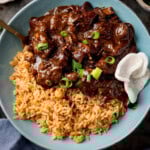 Close up square image of Chinese beef curry and rice in a blue bowl, garnished with chopped spring onions a couple of prawn crackers.
