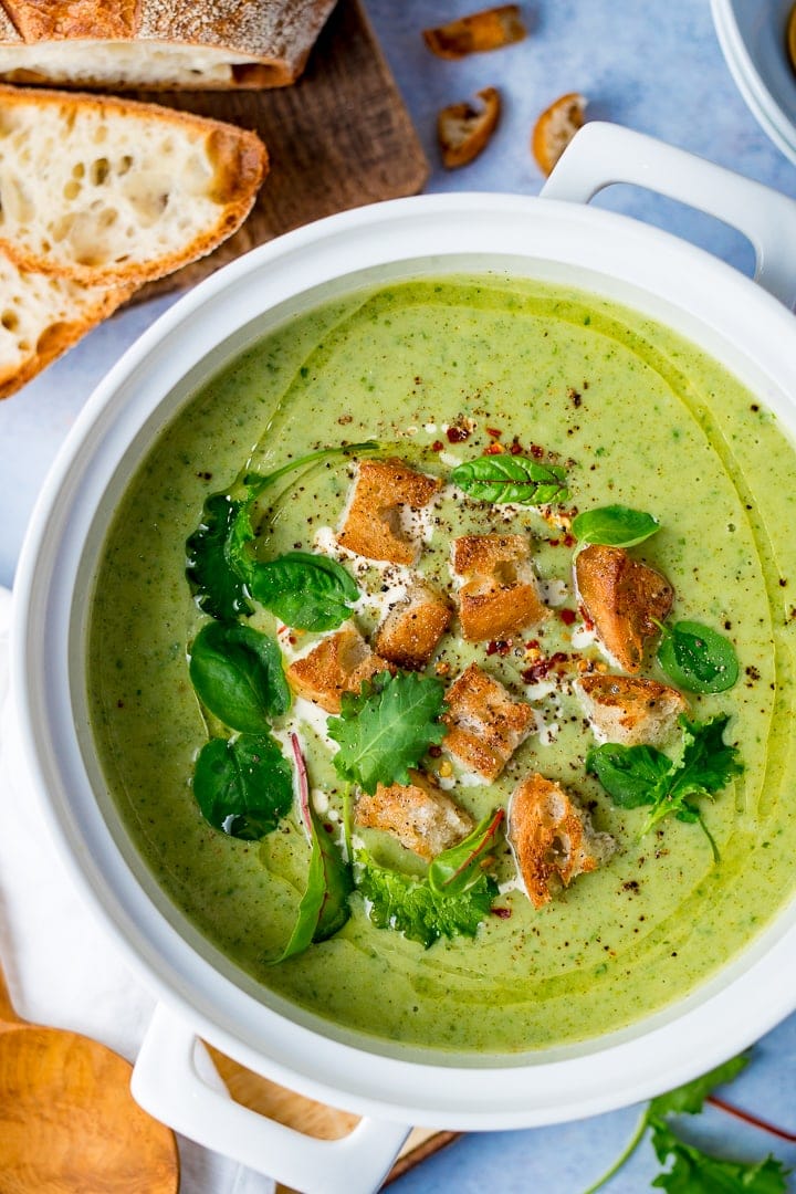 Large pot of broccoli soup topped with croutons and baby salad leaves