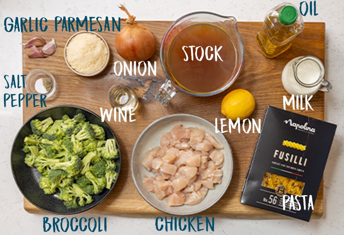 Ingredients for chicken and broccoli pasta on a wooden board.