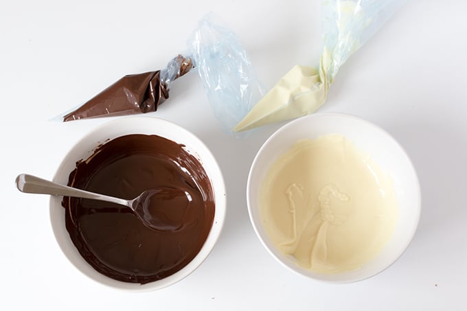 2 bowls, one with melted white chocolate and one with melted dark chocolate.  the dark chocolate bowl has a spoon sticking out of it.