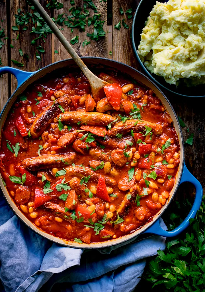 Sausage and bean casserole in a blue pan on wooden background