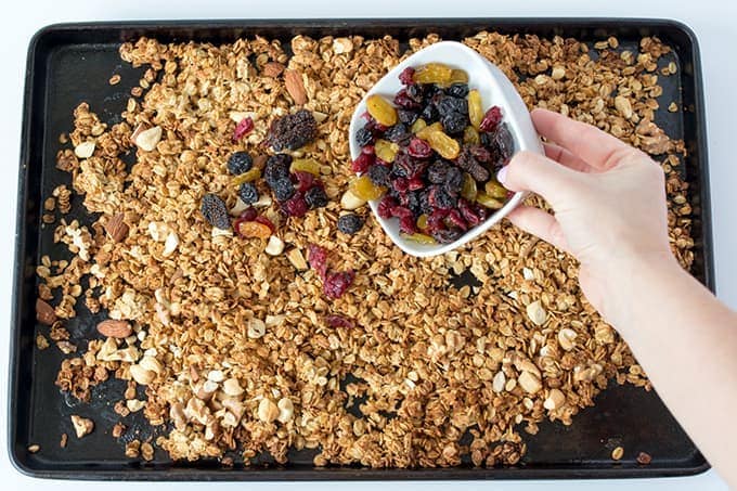 dried fruits being tipped onto a tray of granola