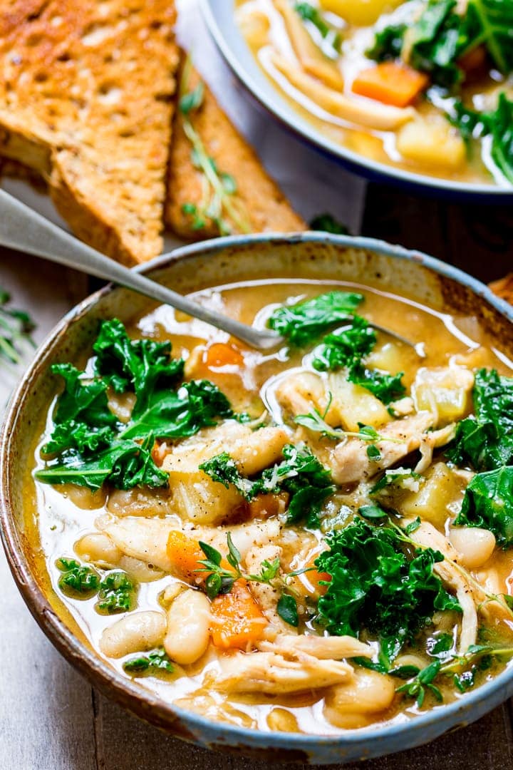 Tuscan Style Chicken Soup in a stone bowl with toast and another bowl of soup in the background