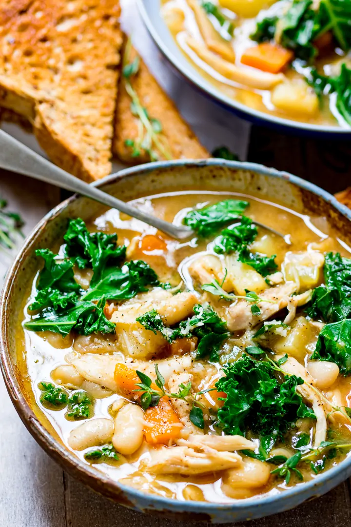 Tuscan Style Chicken Soup in a stone bowl with toast and another bowl of soup in the background