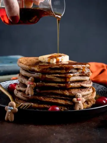 Maple Syrup being poured onto a stack of gingerbread pancakes.