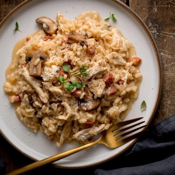 Overhead photo of leftover turkey risotto on a white plate, dressed with a sprig of thyme and with a gold fork.