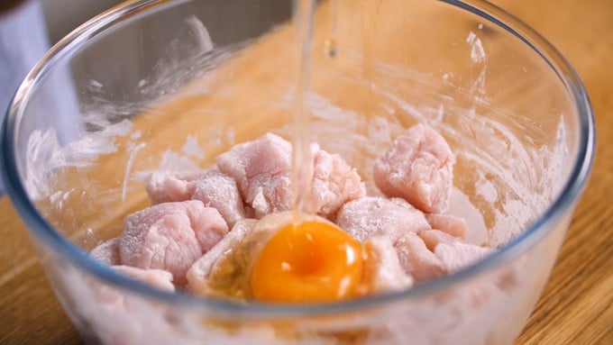 Bowl with flour dusted chicken pieces and a raw egg