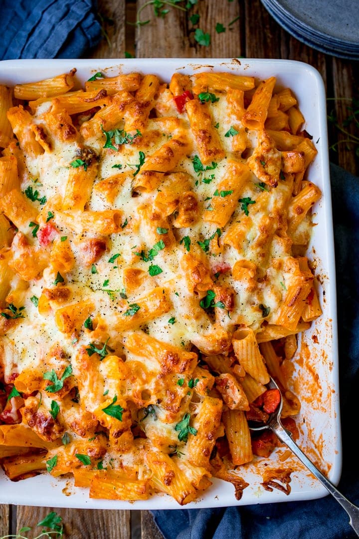 Portrait photo of Cheesy Pasta Bake With Chicken And Bacon in a glass dish with a knife and fork in the background