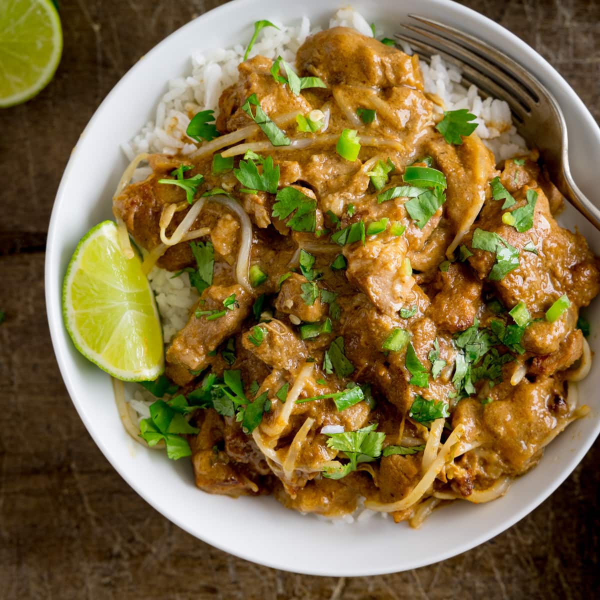 Overhead photo of thai style peanut pork on a bed of rice in a white bowl.