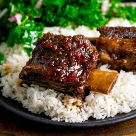 Sticky chilli-glazed short ribs on a bed of rice on a dark plate with kale in the background.