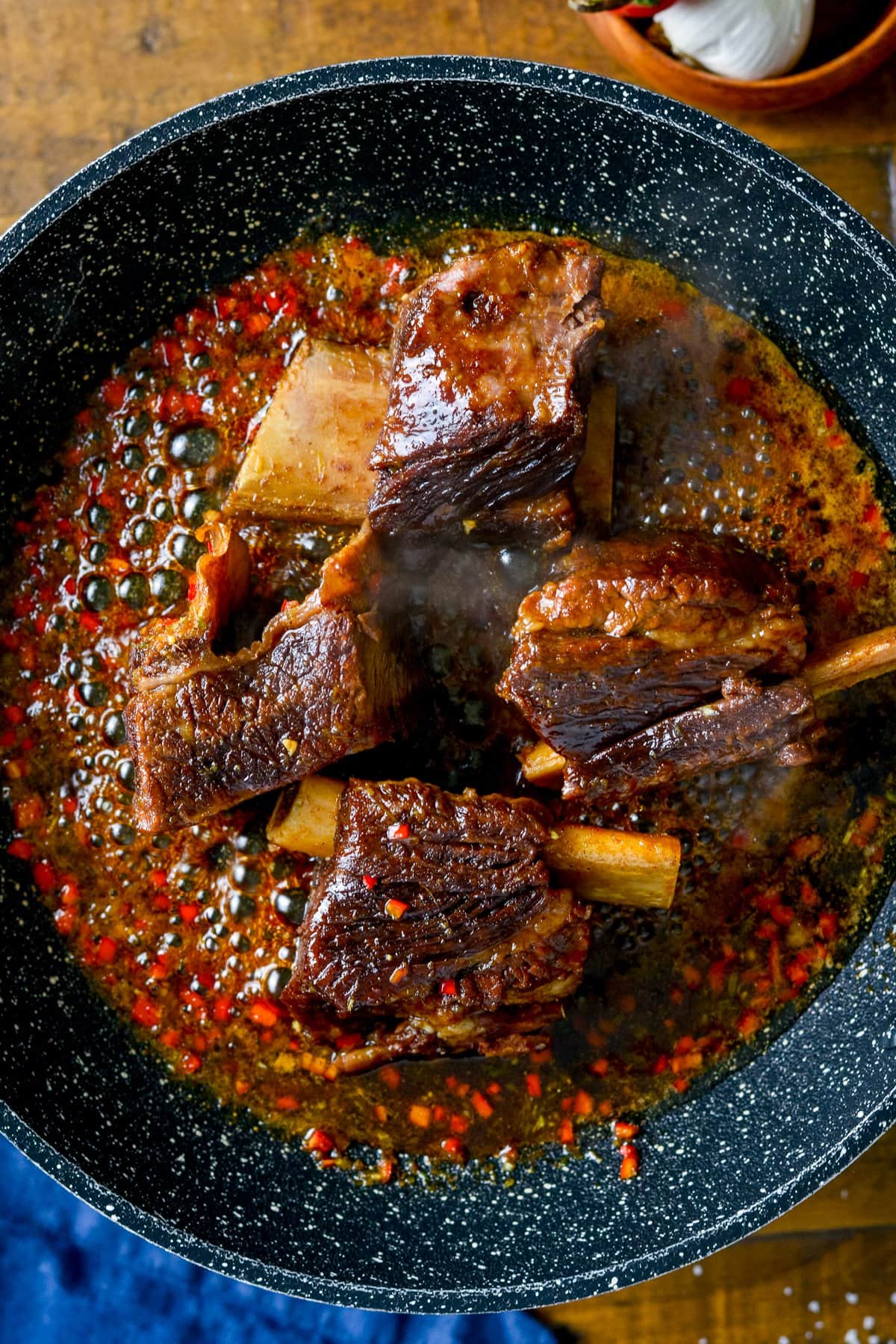 Overhead photo of sticky short ribs in a frying pan with sauce bubbling around the short ribs.