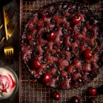 Chocolate Cherry Cake on a wire rack with cherries scattered around.