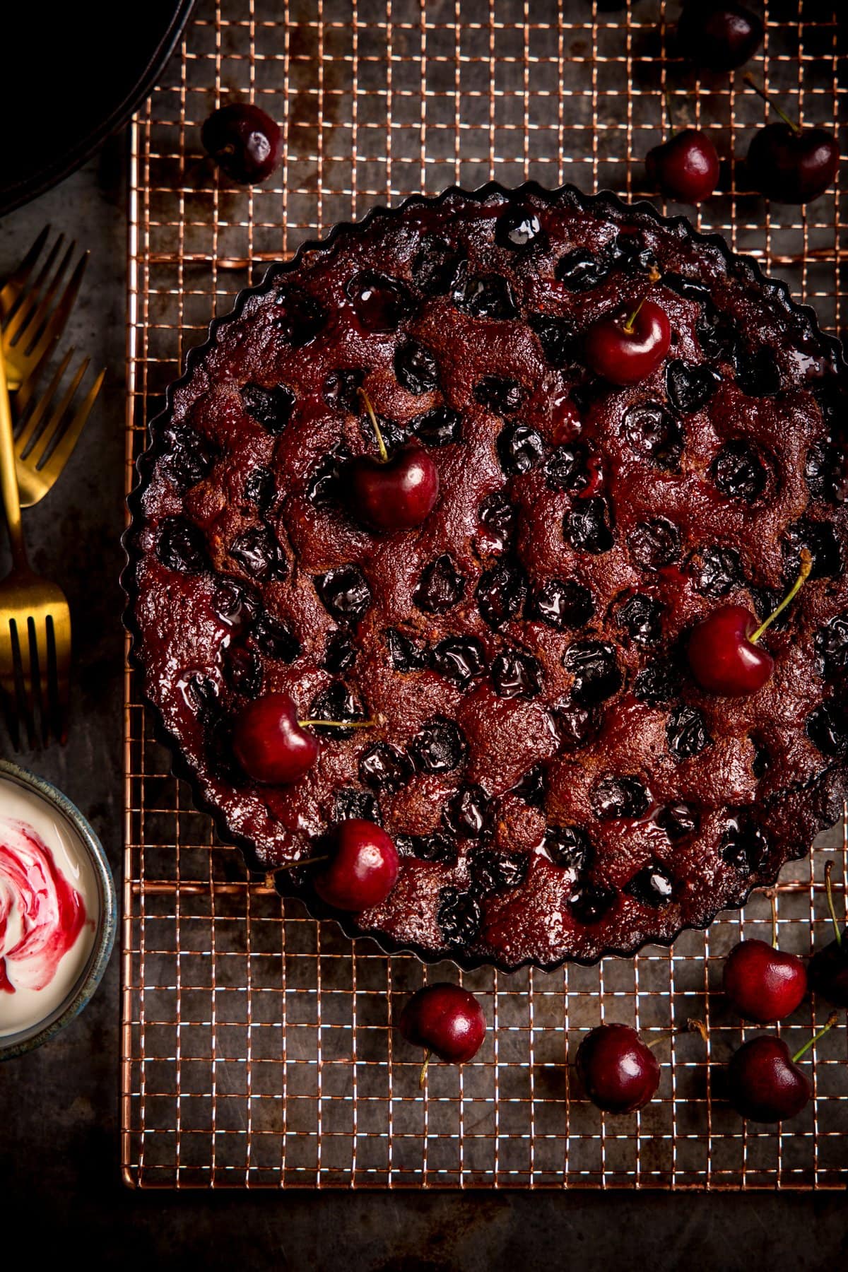 Overhead image of Chocolate Cherry Cake on a wire rack with cherries scattered around.