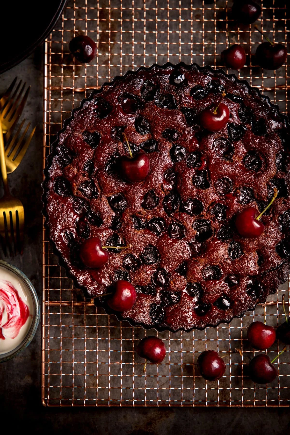 Overhead image of Chocolate Cherry Cake on a wire rack with cherries scattered around.