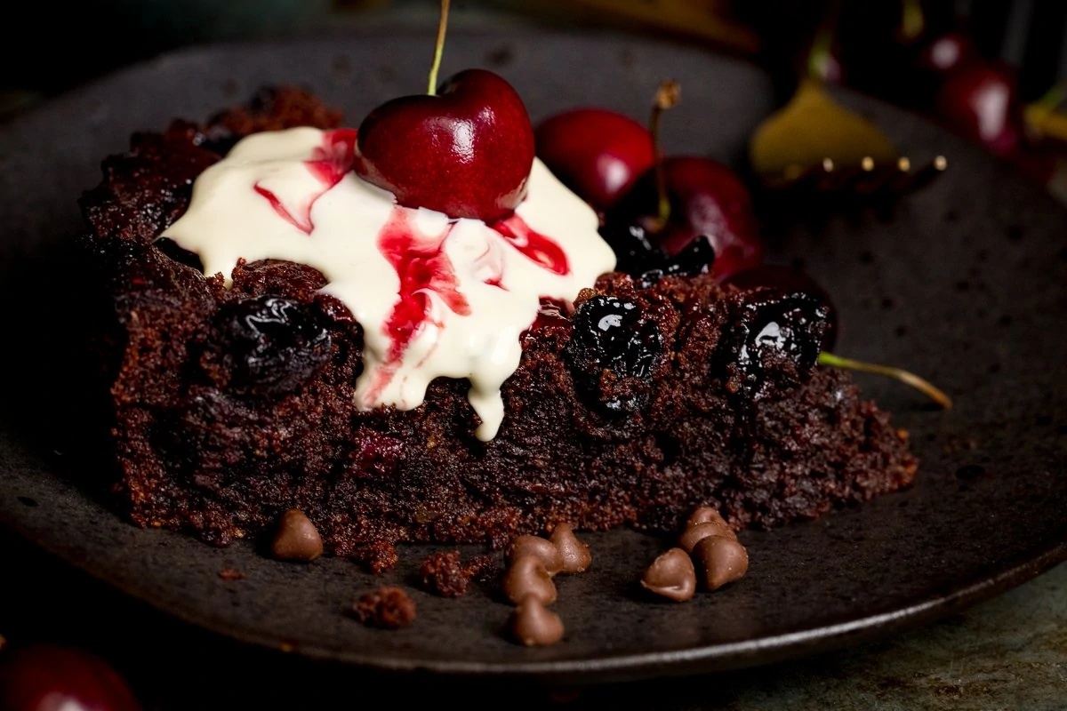 Wide image of chocolate cherry cake slice on a dark plate.